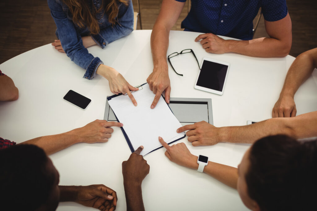 Diverse set of people at a table pointing at a set of work papers.