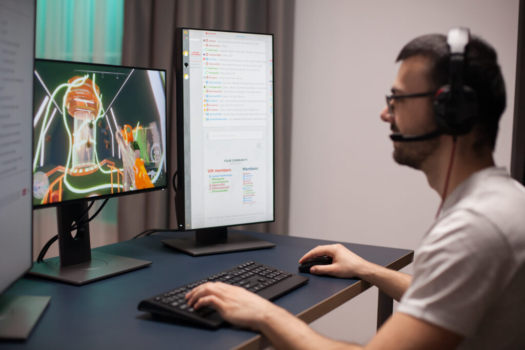 Programmer with headphones looking at two computer screens at home