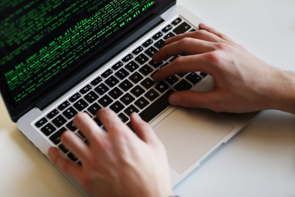 Hands on computer with strings of code on the screen.